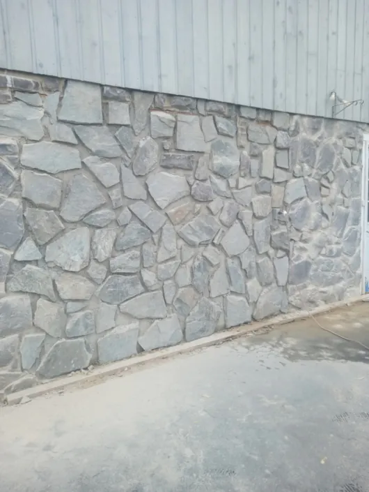 Gray fieldstone veneer wall beside a paved driveway