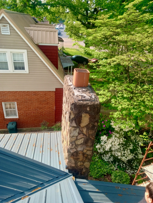 Natural stone chimney with a clay flue above a metal roof