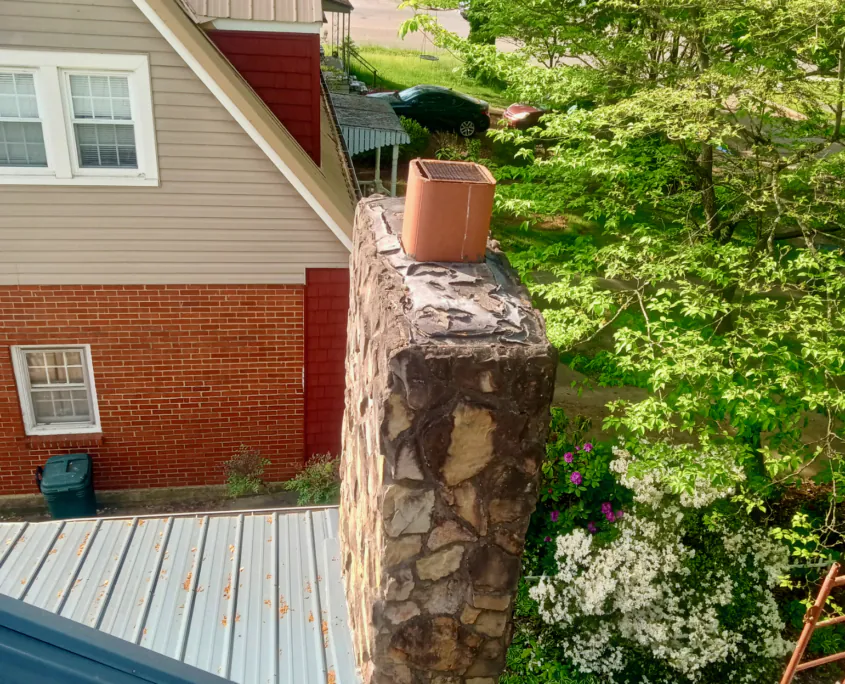 Natural stone chimney with a clay flue above a metal roof