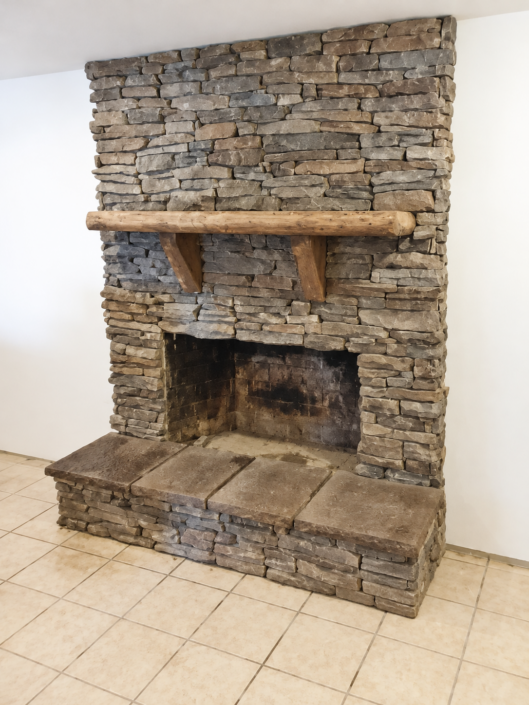 Stone fireplace with timber mantel and raised stone hearth by Hudson Stoneworks