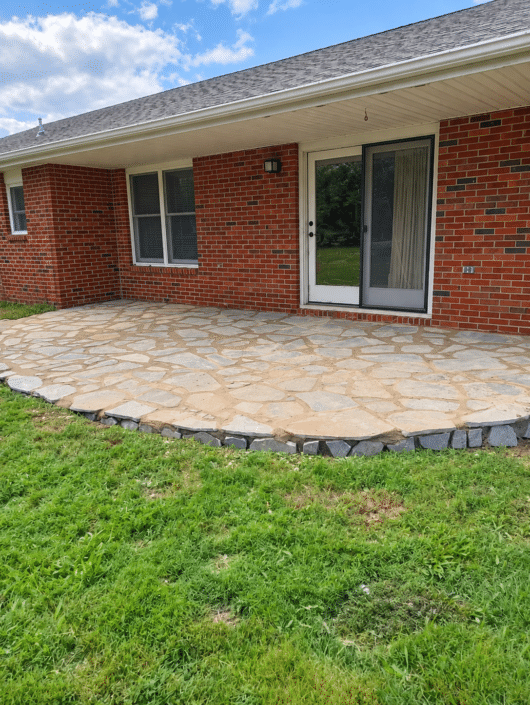 Finished curved flagstone patio with dark stone edging beside a brick house
