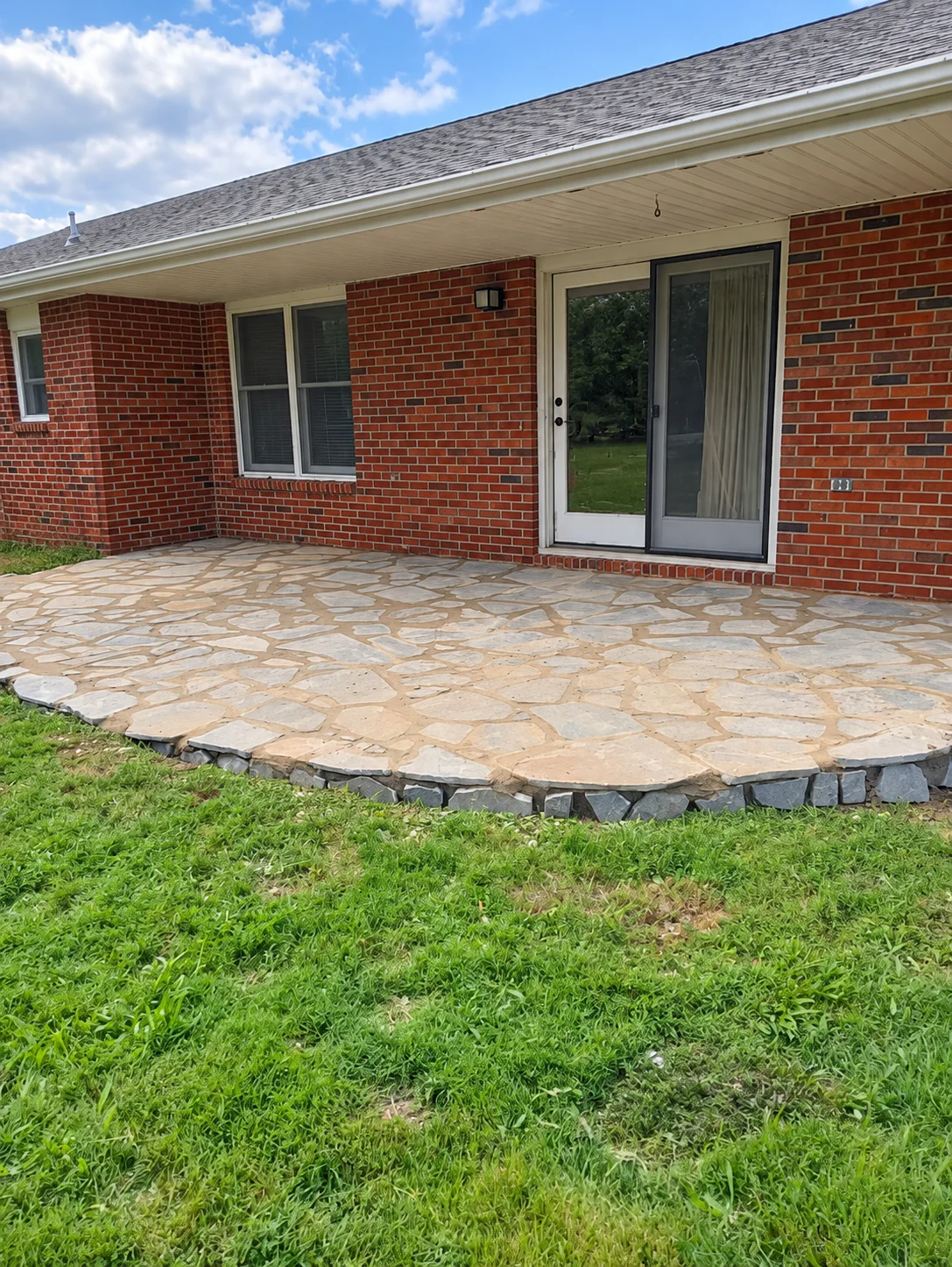 Finished curved flagstone patio with dark stone edging beside a brick house