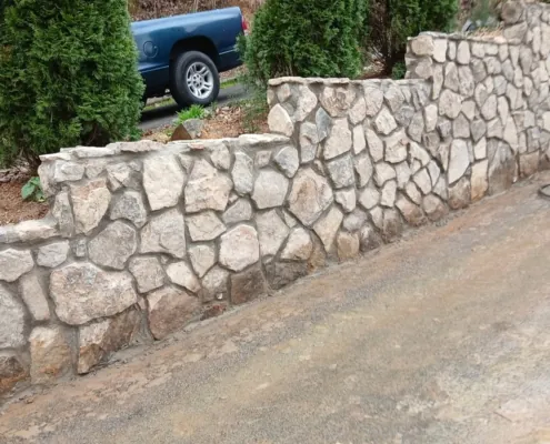 Stepped natural stone retaining wall beside a driveway