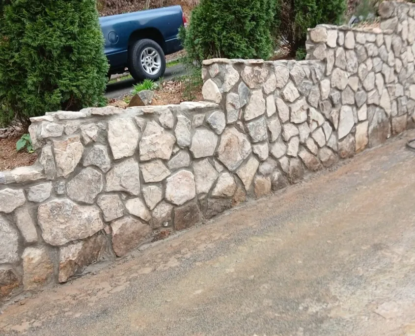 Stepped natural stone retaining wall beside a driveway by Hudson Stoneworks