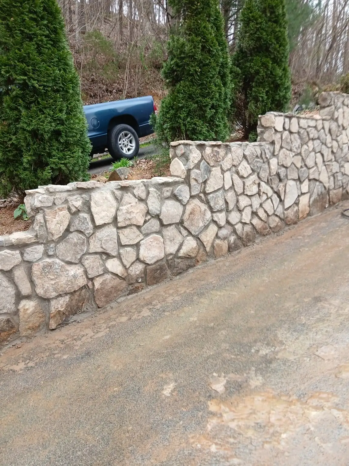 Stepped natural stone retaining wall beside a driveway